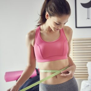 Slim woman measuring her waist at home