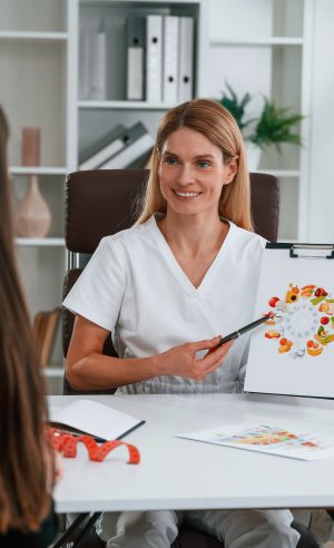 Doctor is showing image that is about vitamins and food. Young woman at a nutritionist's appointment